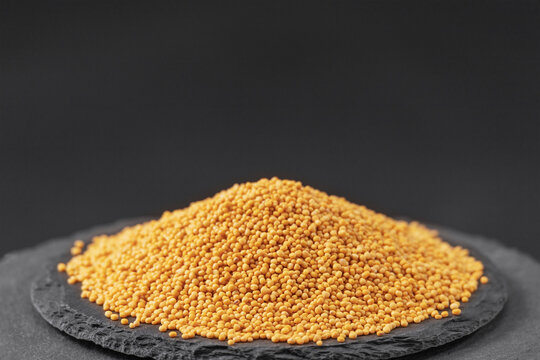 yellow mustard seed known as Sinapis alba on a black slate stone tray