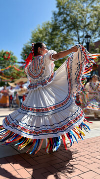 Latina folkloric dancer in a vibrant embroidered dress spinning at an outdoor hispanic heritage month festival rear view with the wide ruffled skirt fanned out in motion blur colorful