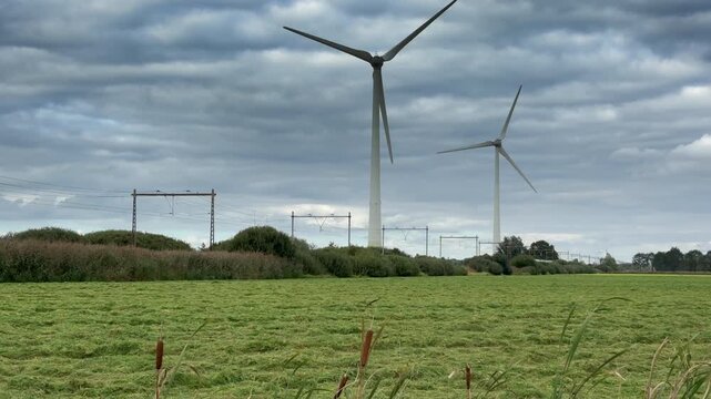 A yellow and blue intercity passenger train of the Nederlandse Spoorwegen NS travels along wind turbines producing sustainable energy.