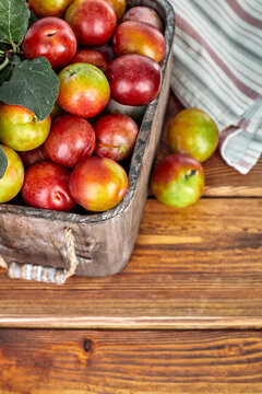 Fresh plum fruits in rustic wooden basket with green leaves. Autumn harvest crops on the old wood table background