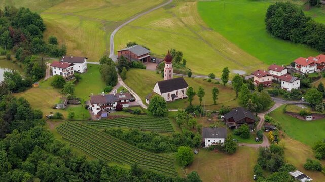 Village church and houses beside neat rows of hillside crops in Dolomites, South Tyrol, Italy