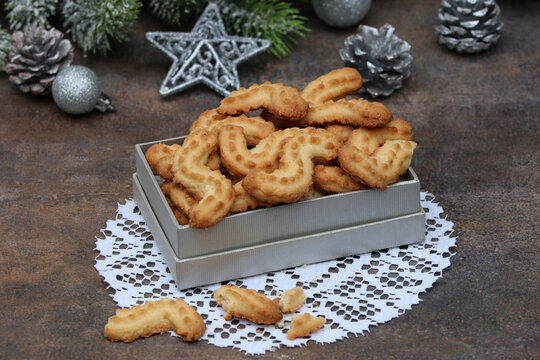 Traditionelles Spritzgeb&auml;ck zur Weihnachts und Adventszeit in einer silbernen Geschenkschachtel auf einem wei&szlig;en Spitzendeckchen.
