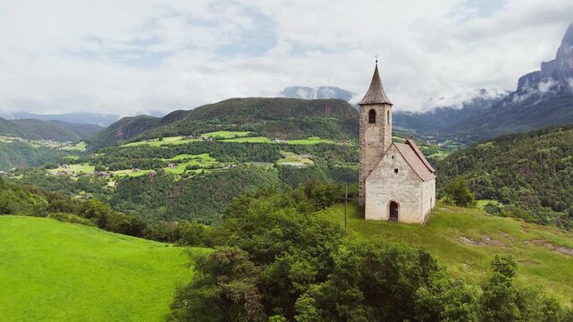 Chapel in Dolomites, South Tyrol, Italy on hill with valley and forest landscape, aerial view