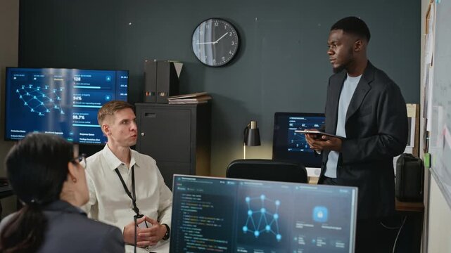 African American young adult man holding digital tablet presenting cybersecurity data to diverse software team in office. Ideal for corporate software training videos and tech enterprise promotions