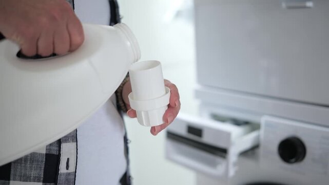 Adult hands twist open white laundry detergent bottle. Washing machine drawer waits nearby.