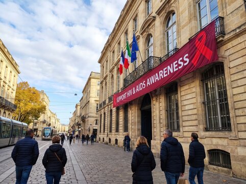 People walking on a historic European street with a large red banner supporting HIV and AIDS awareness