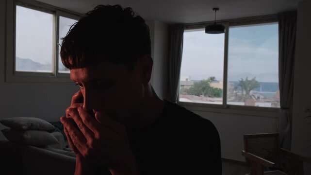 Secretive man having a discreet phone conversation at home, speaking quietly and covering his mouth, carefully hiding sensitive information while maintaining privacy in a dark cinematic interior