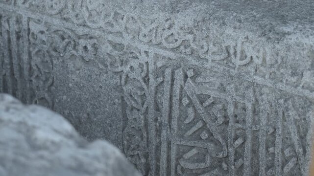 Weathered gray carved stone surface with dense ornamental script relief, shallow focus, blurred foreground, and muted historic texture framed by soft beige edge