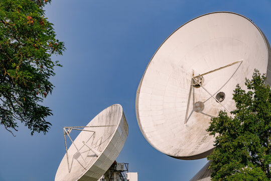 Two large white satellite dishes pointing at the sky against deep blue background, telecommunications, satellite ground station, data transmission and global communication concept