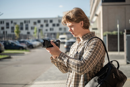 Young photographer checking settings or reviewing images on a digital camera outdoors in the city, representing practical photography training, camera skills and World Photography Day.