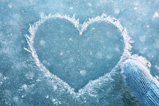 Heart shape drawn on frozen window with blue knitted mitten winter
