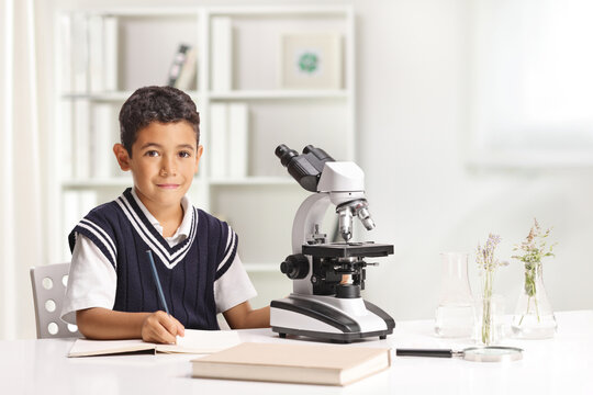 Boy writing homework and doing a research on plants with a microscope