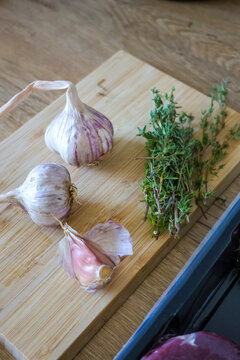 Fresh ingredients including garlic and herbs prepared on a wooden countertop in a modern kitchen before cooking.