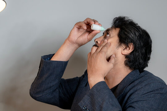 A young office worker applies eye drops to relieve dry and irritated eyes after staring at a computer screen for a long period of time.