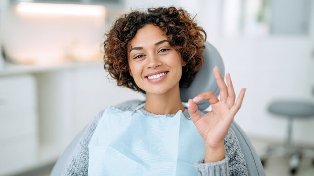 Young woman client satisfied with dental treatment showing perfect smile and ok gesture in dentist office