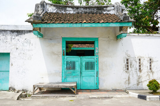 Vintage Chinese Peranakan style entrance gate with green wooden doors, weathered white wall, and tiled roof in Lasem heritage old town, Central Java, Indonesia, reflecting rich cultural history.
