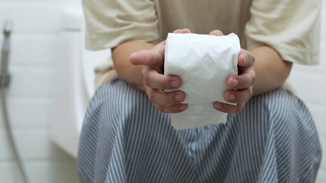 portrait of a man suffers from diarrhea his stomach painful. ache and problem. hand hold tissue paper roll in front of toilet bowl. constipation in bathroom. Hygiene, health care concept.