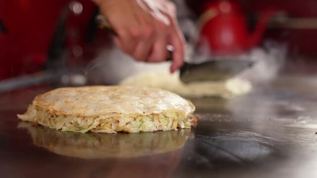 Yakisoba noodles sizzling and steaming on a hot teppanyaki griddle for Hiroshima style okonomiyaki, spread by the chef. Japanese food cooking, static front shot, real time.