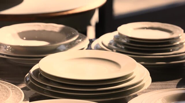 Close up of stacked white porcelain plates glowing in warm sunlight on dark table