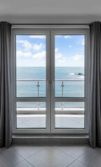 Fototapeta premium A modern glass balcony door with grey curtains frames a scenic view of the ocean under a blue sky.