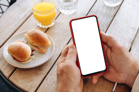 Mockup man's hand holding using smart phone with white blank screen POV at coffee shop, mobile app design and advertising, online marketing	