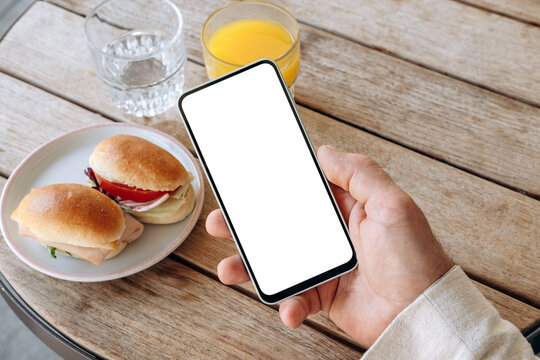 Mockup man's hand holding using smart phone with white blank screen POV at coffee shop, mobile app design and advertising, online marketing	