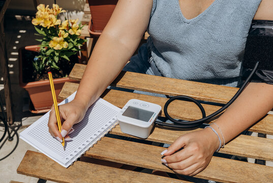 Woman Taking Blood Pressure Reading and Recording Measurements in Notebook on Outdoor Patio