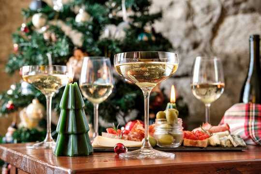 Festive Holiday Table With White Wine Glasses, Cheese Board, Olives and Christmas Tree Decorations