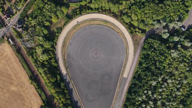 High altitude perspective looking down at a specialized automotive test track surrounded by dense green woodland and fields under bright daylight conditions