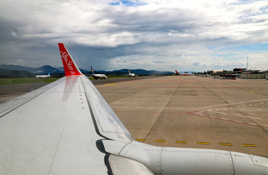 View of Milan Bergamo Airport tarmac and terminal buildings from the wing of an AlbaStar airplane prior to takeoff.