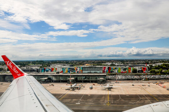 View of Milan Bergamo Airport tarmac and terminal buildings from the wing of an AlbaStar airplane prior to takeoff.