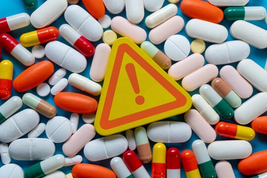 Warning sign with a red exclamation mark and a colorful medical pills. Drug safety, medication side effects, overdose risks, and pharmaceutical contraindications concept.