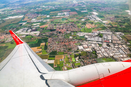 An airplane passenger perspective capturing patchwork fields and suburban landscapes below during flight ascent over northern Italy.