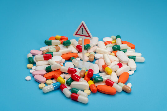 A red exclamation mark and a scattered pile of assorted colorful medical pills. Drug safety, medication contraindications, and pharmaceutical risk concept.