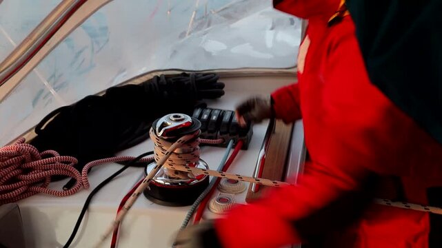 A man in the yacht cockpit loops a rope around the drum of an electric winch with a servo motor 
