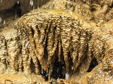 Water Dripping Over Golden Limestone Rock Formations in a Cave