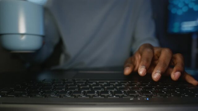 African American young adult man rapidly typing on laptop keyboard while drinking coffee in cybersecurity office. Perfect for software engineering ads, tech training videos or promos