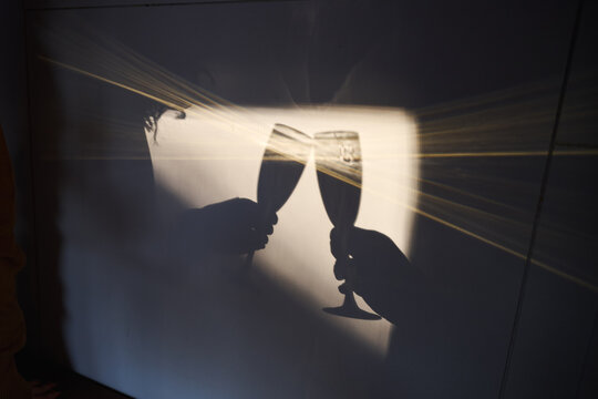 Silhouette of two people clinking champagne glasses against light. Celebration, toast, party mood