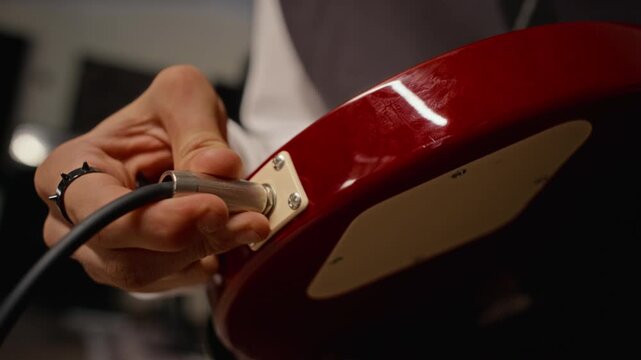 Caucasian teenager inserting audio cable into electric guitar jack during rehearsal. Footage suitable for music education, audio equipment advertising, and sound engineering videos