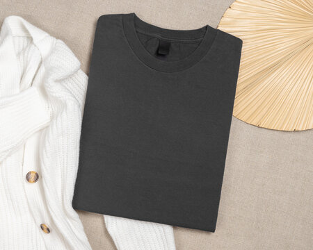 Dark grey folded t-shirt mockup near knitted cardigan and palm leaf, template for print on demand
