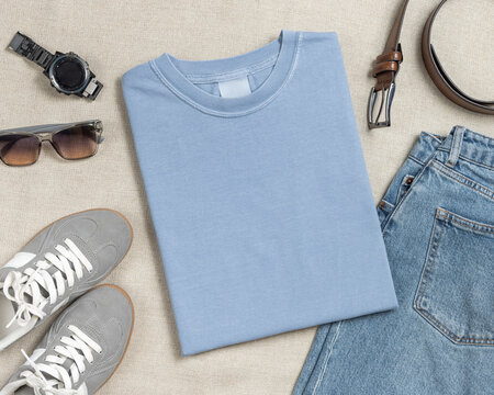 Blank light blue folded unisex t-shirt mockup, crewneck flat lay with jeans and mens accessories