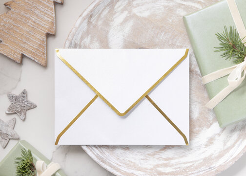 Christmas envelope mockup on wooden plate near sage green gift box and rustic decor