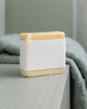 Beige handmade soap mockup with blank label near sage green towel in bathroom, unbranded packaging