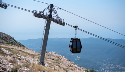 Modern black gondola cabin hangs from a cable line near a steel support tower on a mountain slope © Denis Renkas