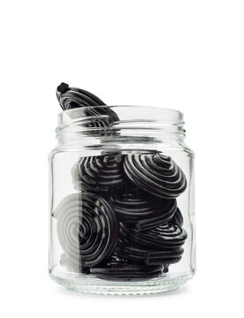 Liquorice candy wheels into small glass jar, isolated on white background.