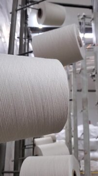 White yarn cones feeding into circular knitting machine in textile factory,.
yarn spools in garment manufacturing
