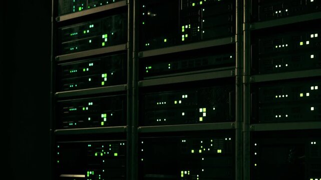 In a darkened server room, rows of data racks illuminate with vibrant green lights.