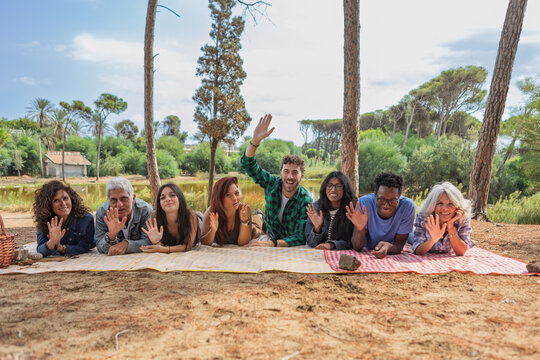 Smiling friends lying in a row on picnic blankets waving at camera
