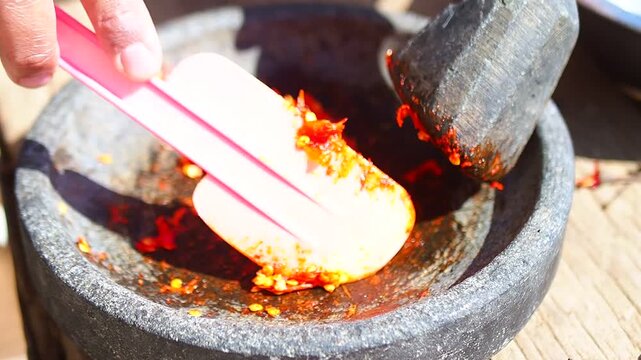 Hand Scraping Ground Red Chilies from Traditional Stone Mortar with Pink Spatula