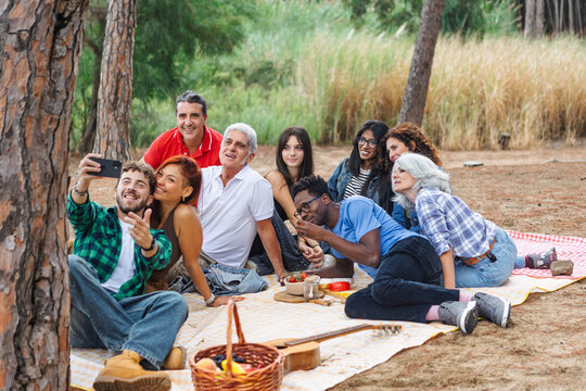 Young man taking a selfie with diverse friends at a forest picnic
